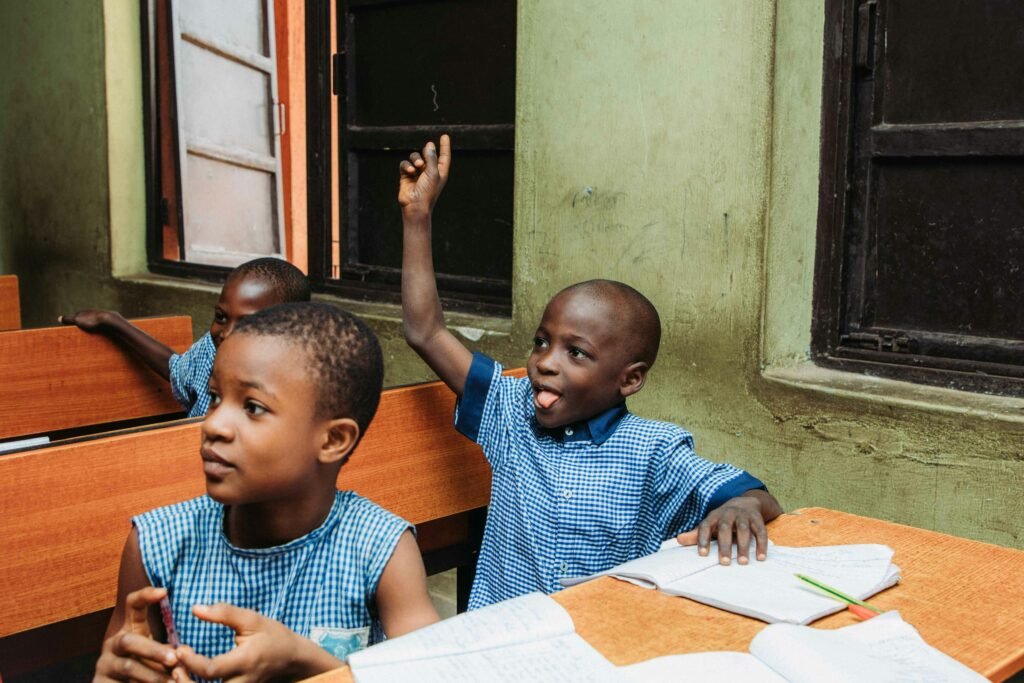 Projets Two young boys in a classroom, one raising his hand with enthusiasm.